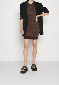 Robe en tricot marron avec un motif géométrique, associée à un blazer noir. Des sandales à plateforme noires avec des boucles complètent le look.
