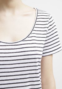 Camiseta a rayas en blanco y gris, con escote redondo y mangas cortas, confeccionada en una suave tela de textura lisa.