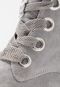 Stivale in suede grigio con occhielli in metallo argentato e lacci in rete testurizzata, con un bordo curvo liscio alla suola e dettagli di cucitura.