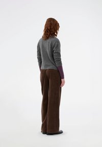 Grauer Pullover mit hochgekrempelten Ärmeln, kombiniert mit braunen Cordstoff-Hosen im weit geschnittenen Stil. Die glatte Strickstruktur steht im Kontrast zu dem gerippten Hosen-Design.