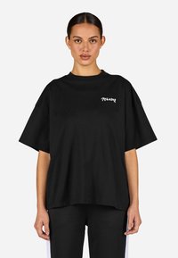 Czarna, oversize koszulka z bawełny, z okrągłym dekoltem i krótkimi rękawami, z napisem "TEGADOR" wykonanym na biało po lewej stronie klatki piersiowej.