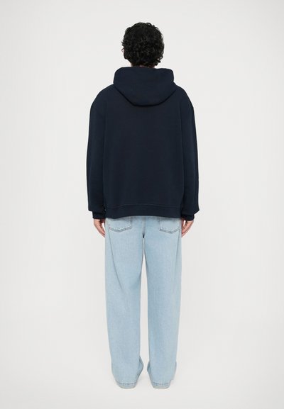 Navyblaues oversized Hoodie mit verstellbarem Kapuzenzug und gerippten Bündchen, kombiniert mit hellblauen weit geschnittenen Jeans, die eine entspannte Passform zeigen.
