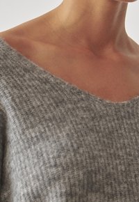 Zbliżenie na szyję i górną część klatki piersiowej osoby ubraną w szaro dzianinowy sweter o szerokim dekolcie.