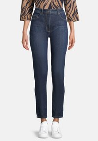 Mörkblå högmidjade jeans med slim fit, femficksdesign och subtil textur, i kombination med vita sneakers.