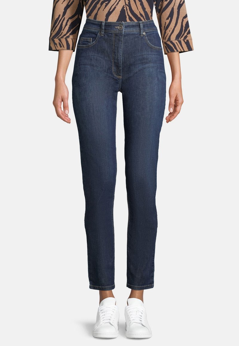 Mörkblå högmidjade jeans med slim fit, femficksdesign och subtil textur, i kombination med vita sneakers.