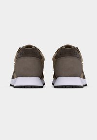 Ζευγάρι μπεζ και καφέ αθλητικά παπούτσια Converse, εμφανιζόμενα από πίσω, με λευκές σόλες και την επωνυμία "CONVERSE" στην ετικέτα της φτέρνας.