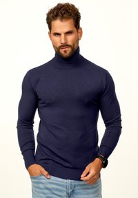 Marineblauer Rollkragenpullover aus weichem Strickmaterial, mit langen Ärmeln und geripptem Saum. Trägt er mit hellblauen Jeans und einer Uhr.