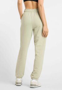 Light green, elastic-waist joggers with tapered cuffs. Smooth texture, subtle detail, worn with white and gray sneakers.