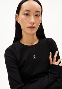 Schwarzes, geripptes Langarmtop mit kleinem weißen Logo auf der Brust, rundem Halsausschnitt und taillierten Ärmeln.