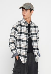 Plaid flanelinė marškiniai baltos, juodos ir rudos spalvų; turi mygtukų užsegimą priekyje ir mėlynas džinsinio stiliaus rankoves. Sukombinuota su juoda marškinėliais su grafika.