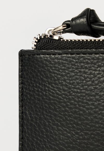 Róg czarnej skórzanej torby o fakturowanej powierzchni. Wyposażony w czarny zamek błyskawiczny oraz srebrne elementy ozdobne, prezentujące minimalistyczny design.