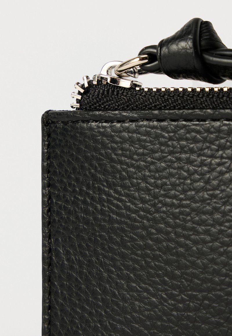 Sort lædertaskehjørne med en tekstureret overflade. Indeholder en sort lynlås og sølvfarvede metaldetaljer, der fremviser et minimalistisk design.