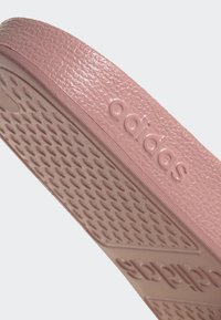 Ružový gumový podrážka s textúrovaným povrchom a diamantovým vzorom, s vyrazeným logom „adidas“. Hladký povrch a zakrivený tvar.