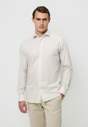 Camisa de botones con rayas blancas, beige claro y delgadas rayas verticales, mangas largas y cuello puntiagudo, combinada con pantalones beige.