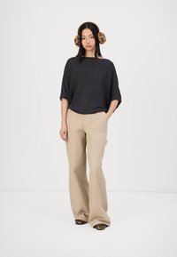Mørkegrå oversized strikket topp, beige vide bukser og brune leopardmønstrede sko. Modellen har på seg brune pelsearmuffer, hender i lommene.