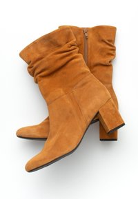 Botas de tobillo de ante marrón con un diseño holgado en la parte superior, punta redondeada y tacón bloque. Incluye una cremallera lateral para facilitar el uso.
