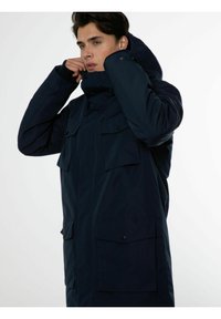 Parka bleu marine, dotée d'une capuche, de multiples poches avant, d'une fermeture éclair et d'un tissu texturé. Conçue pour la chaleur et la fonctionnalité.