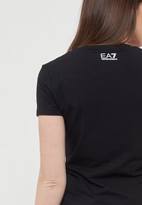 T-shirt nera a maniche corte con scollatura rotonda e un piccolo logo bianco sulla parte posteriore, caratterizzata da una texture in cotone morbido.