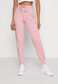 Light pink sweatpants with a drawstring waistband, tapered legs, elastic cuffs, and a small white logo on the left thigh.
