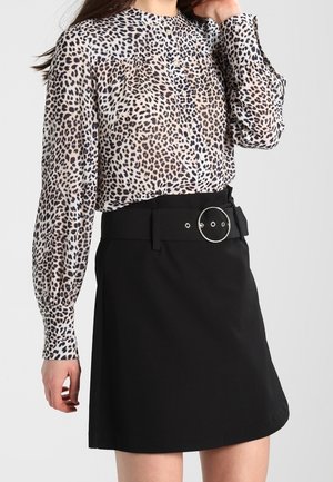 Langärmelige Bluse mit Leopardenmuster, in einen schwarzen A-Linien-Rock gesteckt, der mit einem breiten Gürtel und einer großen runden silbernen Schnalle versehen ist.