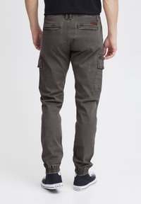 Gray cargo pants with adjustable ankle cuffs, multiple side pockets, and a rear logo patch. Made of durable fabric with a smooth texture.