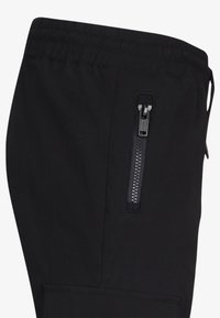 Czarne spodnie wykonane z lekkiego materiału, z elastycznym paskiem w talii, boczną kieszenią na zamek błyskawiczny oraz gładką fakturą z minimalnymi szwami.