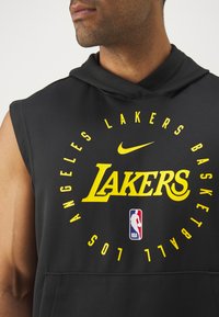 Melnā bezpiedurkņu kapuce ar dzelteno „LAKERS” tekstu apļveida dizainā, ar Nike logo augšpusē un NBA logo apakšā. Mīksta auduma tekstūra.