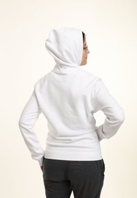 Sudadera blanca con capucha y un corte holgado, puños y cinturilla de canalé. La tela parece suave y lisa sin patrones visibles.