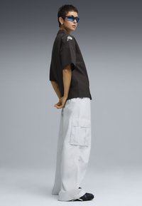 Camisetta nera a maniche corte con logo, pantaloni cargo blu chiaro, occhiali da sole blu e calzature nere. Tessuto morbido e vestibilità ampia.