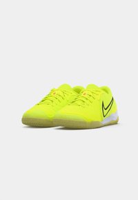 Un paio di vivaci scarpe da atletica low-top di colore giallo neon con il logo swoosh nero e suole texturizzate di colore marrone chiaro su sfondo bianco.