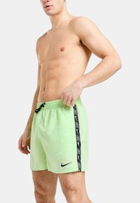 Pantaloni da bagno verde chiaro con accenti neri sui lati, vita con cordoncino e logo Nike. Realizzati in tessuto a asciugatura rapida, taglio fino al ginocchio.