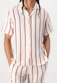 Camisa de botones de manga corta en tela crema con rayas verticales rojas, que presenta un ajuste relajado y un patrón texturizado.