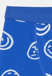 Blå bomulls boxershorts med hvite smiley face-mønstre, en myk elastisk midje, og synlige sømdetaljer.