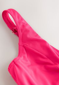 Haut de maillot de bain rose vif avec bretelle réglable et texture de tissu lisse sur fond neutre.