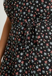 Czarna tkanina z kwiatowym wzorem, w którym znajdują się czerwone, niebieskie i białe kwiaty. Zawiera wiązanie w talii oraz plisowany krój.