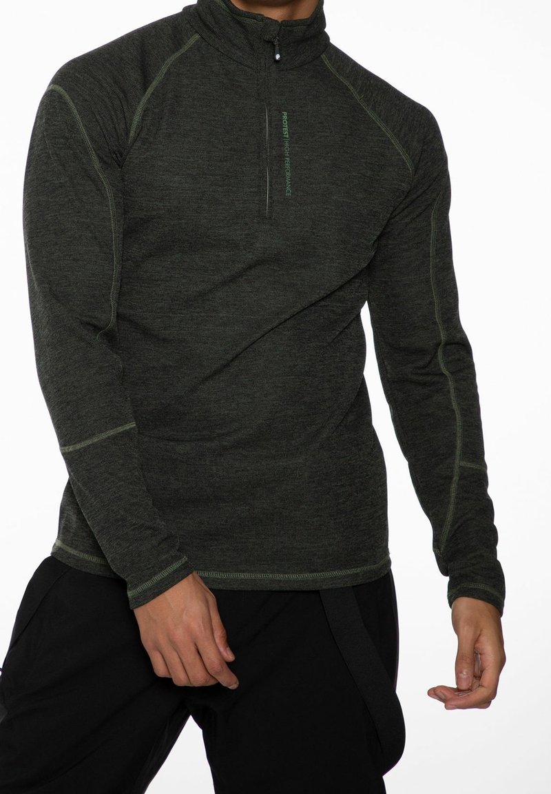 Homme portant un haut de sport gris foncé à manches longues avec fermeture éclair quart de zip et surpiqûres contrastantes, et un pantalon noir, sur fond blanc.