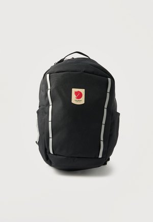 Μαύρο σακίδιο με δύο κάθετες αντανακλαστικές ρίγες και ένα τετράγωνο έμβλημα με λογότυπο κόκκινης αλεπούς στο εμπρόσθιο μέρος, απομονωμένο σε ανοιχτό φόντο.