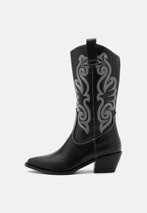 Bottes de cowboy en cuir noir avec un bout pointu, hauteur mi-mollet, ornées d'une broderie argentée délicate et d'un talon empilé.