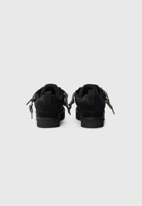 Scarpe in suede nero con accenti in rete, suole piatte e dettagli con zip sui lati. Design pulito con punta arrotondata e parte superiore testurizzata.