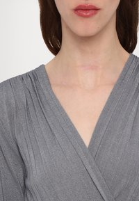 Top gris à enrouler fabriqué à partir d'un tissu texturé avec des rayures verticales. Présente un décolleté en V profond et des fronces aux épaules.