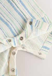 Gros plan d’un tissu à rayures bleu pastel et vert avec des boutons-pression en métal sur un vêtement en coton blanc.