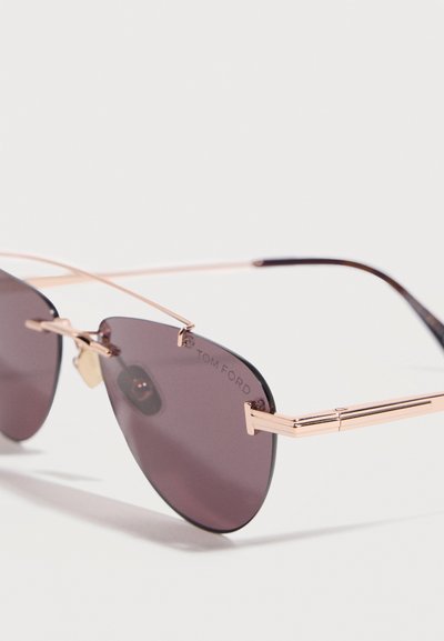 Rimless aviator sunglasses with purple-tinted lenses and thin gold metal temples, featuring a small engraved "Tom Ford" logo on the lens.
