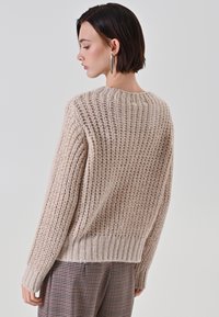 Maglione beige lavorato a maglia con texture a coste, scollo rotondo e maniche lunghe, caratterizzato da una vestibilità comoda e una lunghezza leggermente corta.