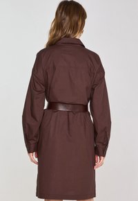 Abito in cotone marrone con maniche lunghe, colletto e vita con cintura. Presenta bottoni sulle maniche e una texture liscia. Vista posteriore mostrata.