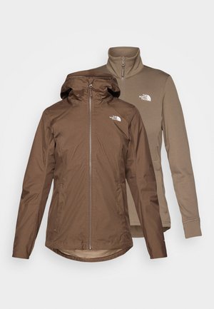 Veste imperméable marron avec capuche amovible, fermeture éclair sur le devant et deux poches latérales. Associée à une couche interne en polaire brun clair.
