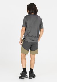 Kortärmad grå sportskjorta i kombination med tvåfärgade shorts i mörkgrått och olivgrönt, med dragsko och dragkedjeficka. Svarta skor.