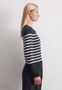 Svart og hvitstripet langermet topp med rund hals, laget av mykt stoff, med kontrasterende horisontale striper og ribbestrikkede mansjetter.