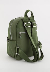 Mochila de nylon verde oliva con dos correas ajustables, herrajes plateados, bolsillos con cremallera en el frente y bolsillos laterales. Textura suave con detalles acolchados.