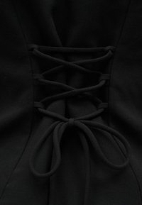 Μαύρο ύφασμα με κορσέ σε στυλ δέσιμο κορδονιών δεμένο σε φιόγκο, που δείχνει πλεγμένους βρόχους και ραφές.