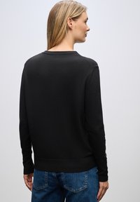 Maglione nero a maniche lunghe in maglia con scollo rotondo e polsini a costine. Tessuto morbido e design semplice e minimalista. Indossato con jeans blu.